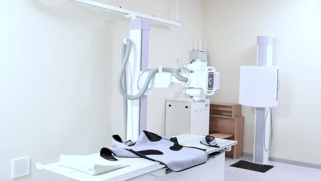 Hospital X-ray machine for fluoroscopy. X-ray department in modern hospital. Radiology room with scan machine with empty bed. Technician adjusting x-ray machine. Scanning chest, heart, lungs in clinic