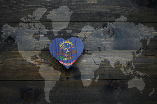 wooden heart with national flag of north dakota state near world map on the wooden background.