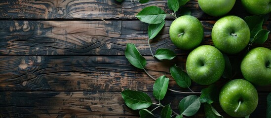 A bunch of fresh green apples with leaves sitting on top of a rustic wooden table.