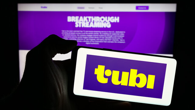 Stuttgart, Germany - 04-08-2024: Person holding mobile phone with logo of American streaming platform company Tubi Inc. in front of business web page. Focus on phone display.