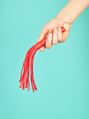 Red whip for adult role play games in woman's hand over turquoise blue background