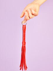 Red whip for adult role play games in woman's hand over violet background