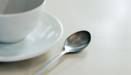 Empty white porcelain coffee cup on a saucer on a white table with a spoon next to it. Copy space