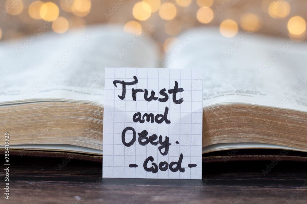 Wall mural trust and obey, god, handwritten quote with open holy bible and bokeh light background. close-up. fa - Wall murals