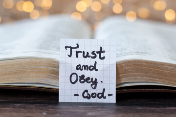 Trust and obey, God, handwritten quote with open holy bible and bokeh light background. Close-up....
