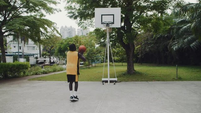 Slow motion of young black male athlete in yellow sportswear playing streetball alone on outdoor court