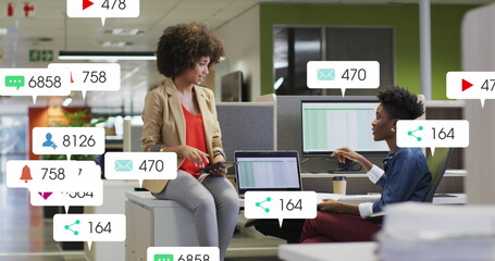 Image of notification bars over diverse female coworkers discussing reports on desk in office