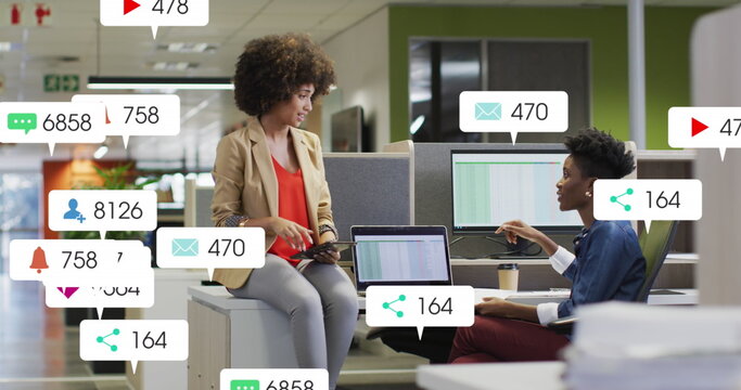 Image of notification bars over diverse female coworkers discussing reports on desk in office