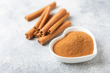 Cinnamon powder in a bowl on a textured wooden background. Spicy spice for baking, desserts and drinks. Fragrant ground cinnamon. Cinnamon stick. Place for text. Copy space.