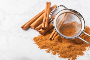Cinnamon powder in a bowl on a textured wooden background. Spicy spice for baking, desserts and drinks. Fragrant ground cinnamon. Cinnamon stick. Place for text. Copy space.