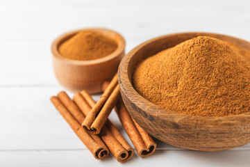 Cinnamon powder in a bowl on a textured wooden background. Spicy spice for baking, desserts and drinks. Fragrant ground cinnamon. Cinnamon stick. Place for text. Copy space.