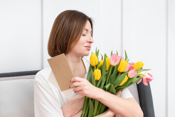 A young beautiful girl received a bouquet of flowers and a congratulatory letter on a wonderful World Women's Day. She sits and reads the letter and thanks the sender