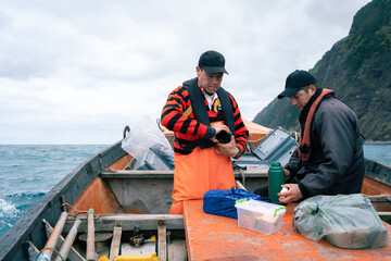 Fishermen drink coffee from a thermos on a boat