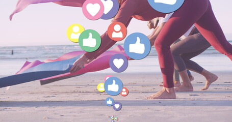 Image of media icons over diverse women with yoga mats at beach