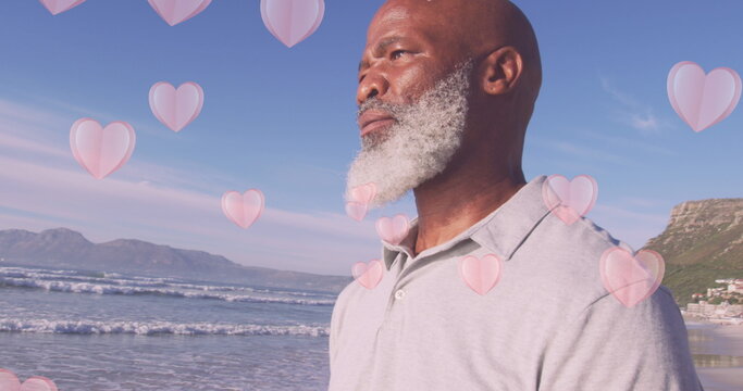 Image of hearts over senior african american man at beach