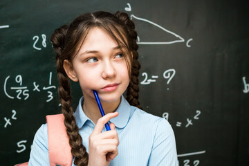A teenage schoolgirl is thinking while standing at the blackboard, a 10-12 year old girl solving a...