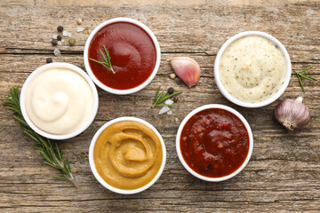 Different tasty sauces in bowls, herbs and spices on wooden table, flat lay