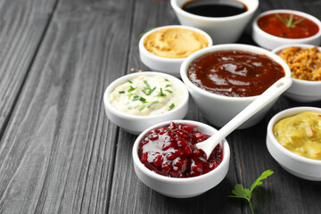 Different tasty sauces in bowls and parsley on black wooden table, closeup. Space for text