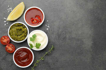 Different tasty sauces in bowls and ingredients on grey table, flat lay. Space for text