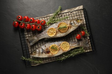 Baked fish with tomatoes, rosemary and lemon on black textured table, top view