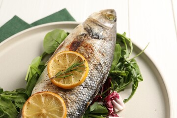 Baked fish with spinach and lemon on white wooden table, closeup