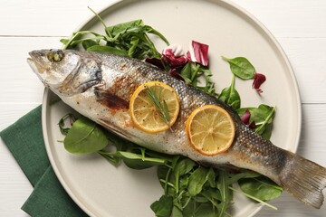 Baked fish with spinach and lemon on white wooden table, top view