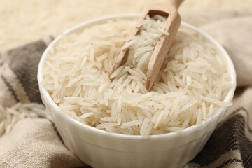 Raw basmati rice in bowl and scoop on cloth, closeup - obrazy, fototapety, plakaty