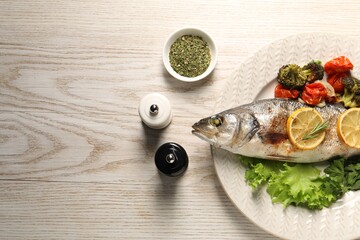 Delicious baked fish and vegetables served on wooden table, flat lay. Space for text