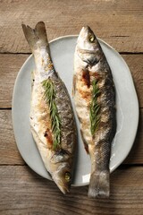 Delicious baked fish and rosemary on wooden table, top view