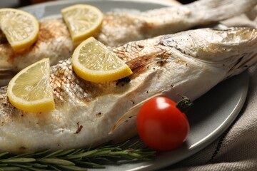 Delicious baked fish, tomato, lemon and rosemary on plate, closeup