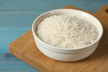 Raw basmati rice in bowl on light blue wooden table, closeup