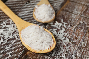Raw basmati rice in spoon on wooden table, closeup