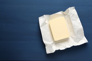 Block of tasty butter in open foil packaging on blue wooden table, top view. Space for text