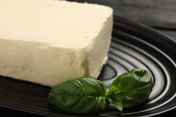 Block of tasty butter and basil on black table, closeup