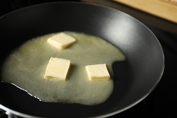 Melting butter in frying pan on black table, closeup