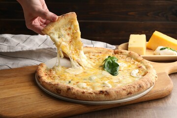 Woman taking piece of delicious cheese pizza at wooden table, closeup