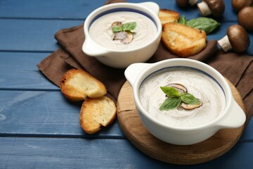 Delicious mushroom soup in ceramic pots and fresh ingredients on blue wooden table. Space for text