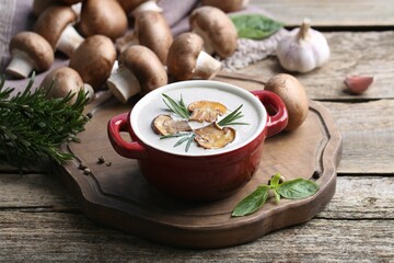 Delicious homemade mushroom soup in ceramic pot and fresh ingredients on wooden table