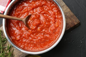 Homemade tomato sauce and spoon in pot on dark textured table, flat lay