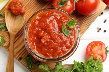 Homemade tomato sauce in jar, spoon and fresh ingredients on white wooden table, flat lay