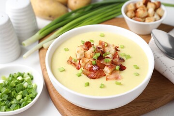 Tasty potato soup with bacon, green onion and croutons in bowl served on white table