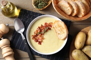 Tasty potato soup with bacon in bowl served on wooden table, flat lay