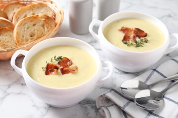 Tasty potato soup with bacon and rosemary in bowls served on white marble table