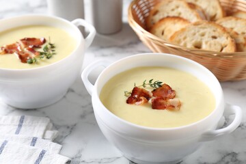 Tasty potato soup with bacon and rosemary in bowls on white marble table, closeup