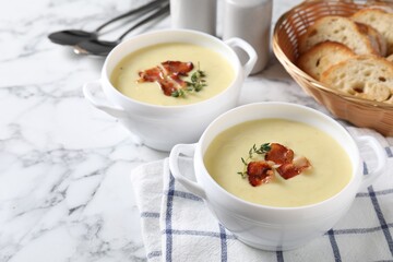 Tasty potato soup with bacon and rosemary in bowls served on white marble table