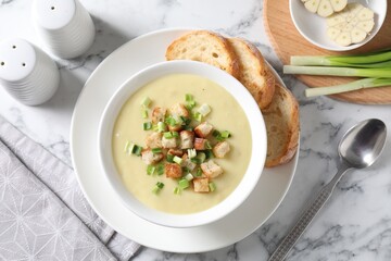 Tasty potato soup with croutons and green onion in bowl served on white marble table, flat lay