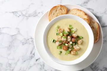 Tasty potato soup with croutons and green onion in bowl on white marble table, top view. Space for text