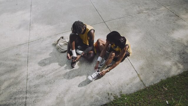 View from above of black male basketballers wearing sneakers sitting on outdoor court and chatting