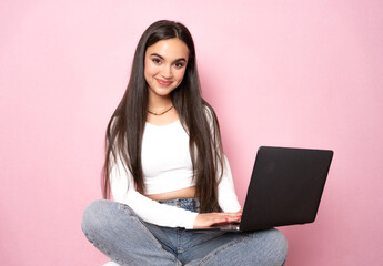 Smart beautiful young girl using laptop pc computer isolated on pink background