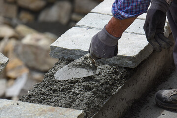 muratore al lavoro cazzuola cemento costruzione muro di sassi pietre  - obrazy, fototapety, plakaty